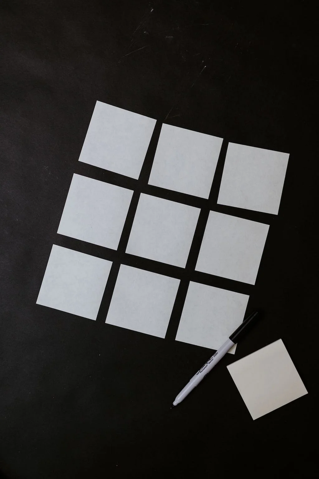 A neat 3x3 grid of blank sticky notes with a marker and a single extra note, arranged on a black background.