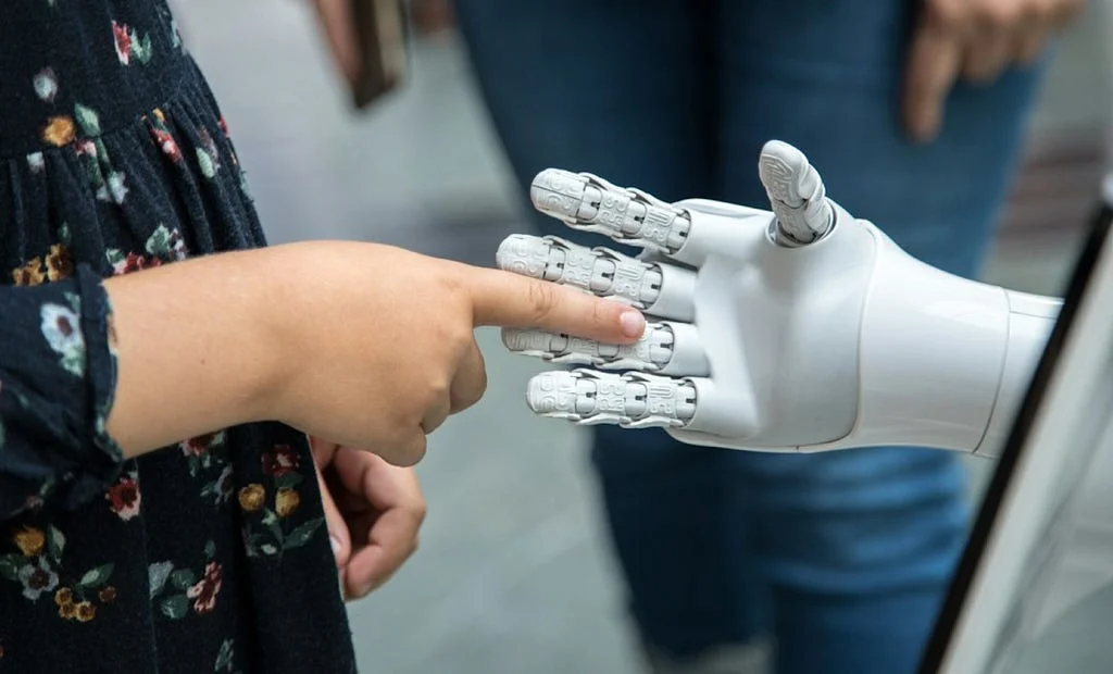 A child's finger touching the extended index finger of a white robotic hand.